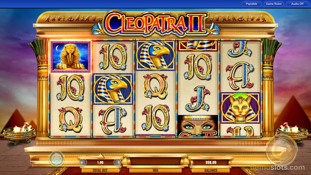 A 5x3 grid of symbols for the Egyptian-themed slot game Cleopatra II is displayed against a sunset background with pyramids and burning braziers.